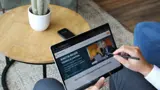 Wijst met een tabletpen naar de tafel en toont zijn eigen website.